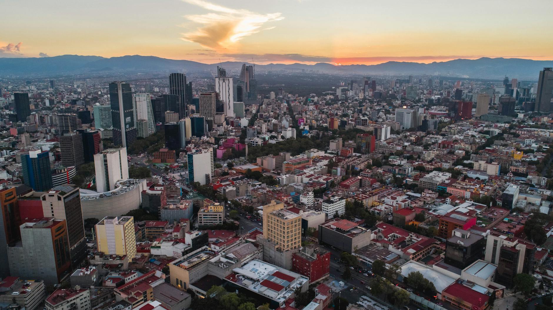 Aerial photograph of modern Latin American city skyline at golden hour, warm teal and navy color grade, soft evening light on glass towers, editorial architectural photography
